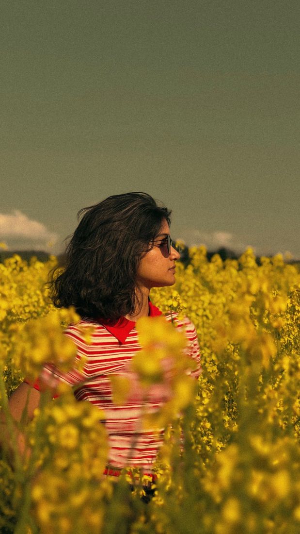 Mulher de blusa listrada vermelha num campo de flores amarelas, imagem parada